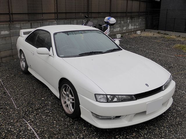  A 1995 Nissan Silvia S14 with a wider, more rounded body, lowered suspension, and aftermarket wheels, parked at a car meet under neon lights.