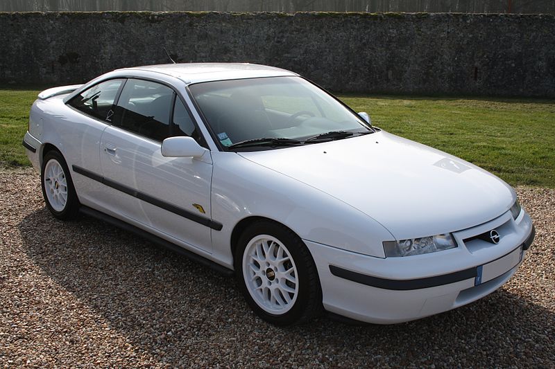 Opel Calibra in a dynamic view, showcasing its sleek and aerodynamic design with slim headlights and sporty silhouette, parked in a scenic setting