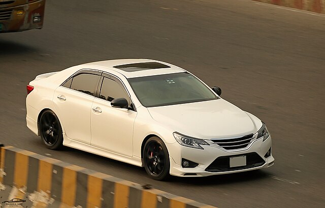 Toyota Mark X driving on the highway with a clear background.